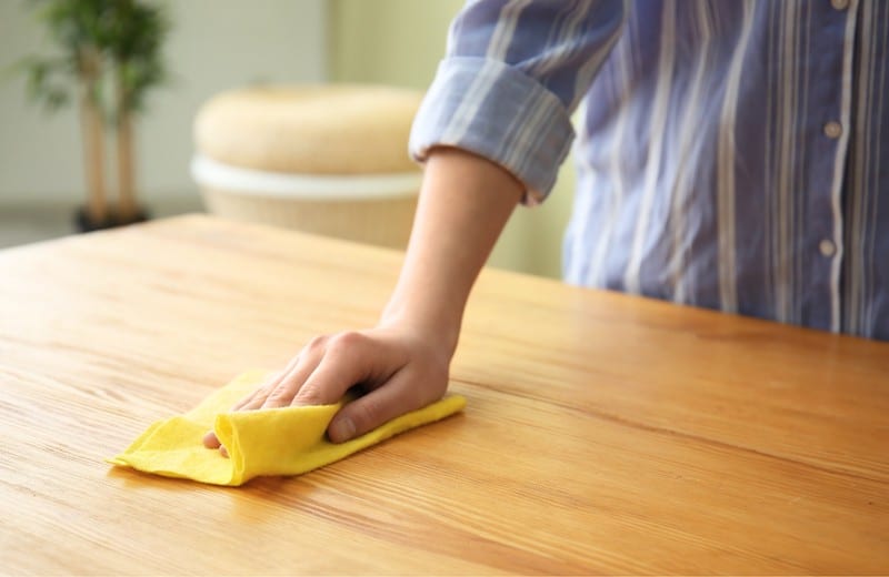 Une femme de ménage qui nettoie une table avec une éponge jaune